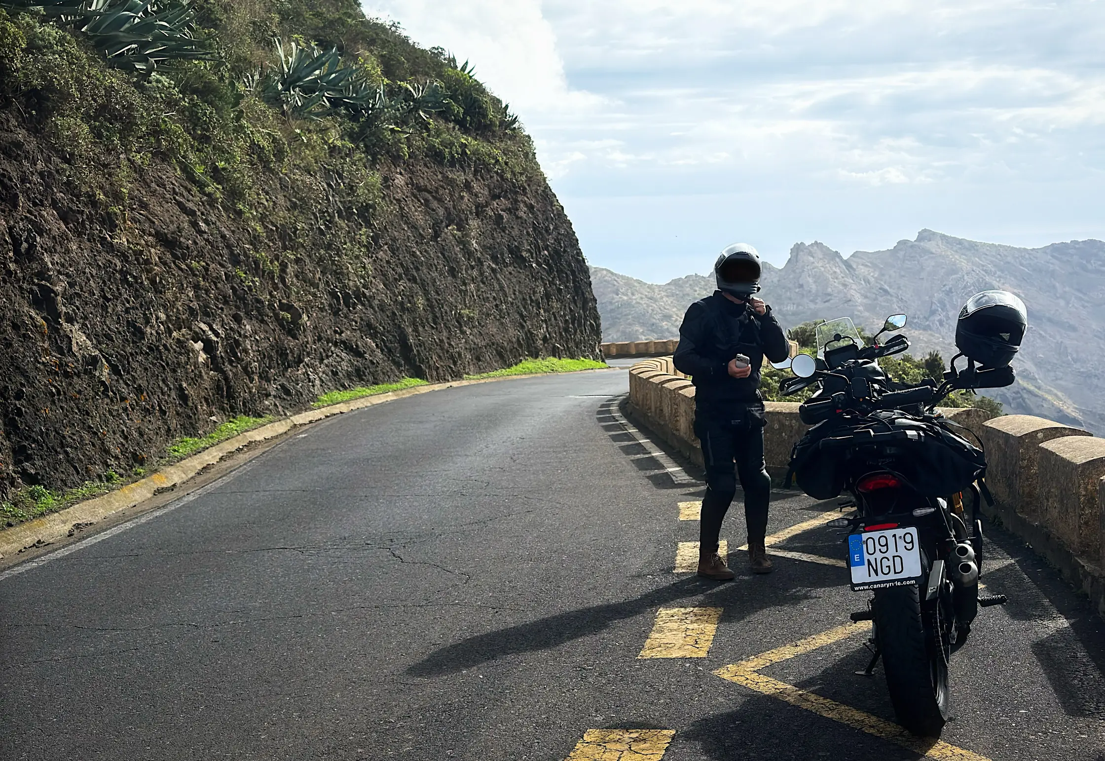 A rider pulling on his helmet beside his motorcycle on a mountain road in Tenerife, ready to ride with ScoutRoute